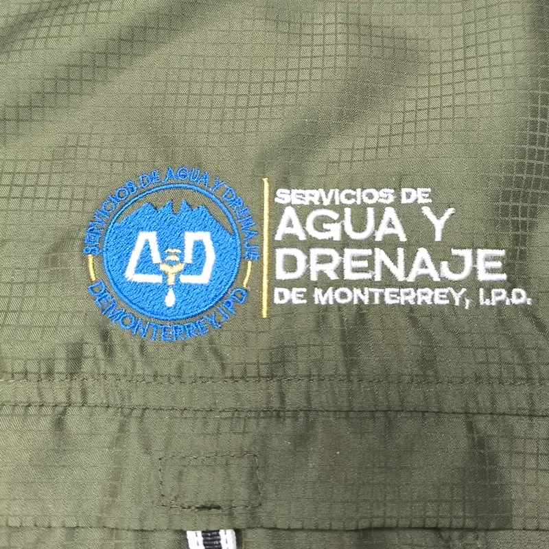 Logotipo bordado en azul y blanco sobre una camisa verde olivo